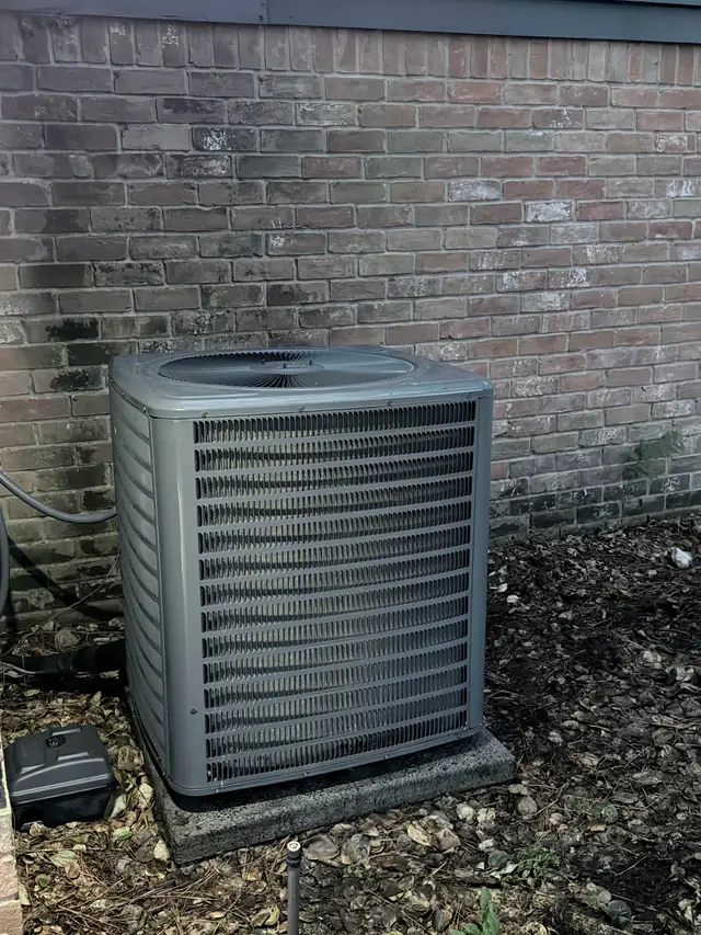 Condenser on its pad against a brick wall